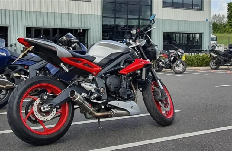 Triumph Street Triple RX motorcycle parked outside a dealership, featuring sporty red alloy wheels and an aggressive streetfighter design