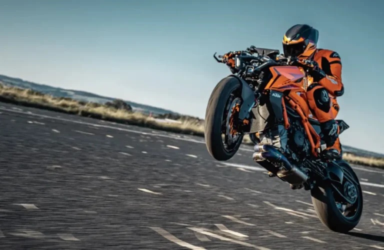 Rider performing a high-speed wheelie on an orange KTM Super Duke, showcasing aggressive power and precision on an open road.